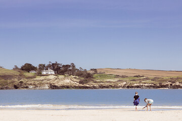 Fototapeta na wymiar Two young children beach combing along the shoreline near Padstow, Cornwall