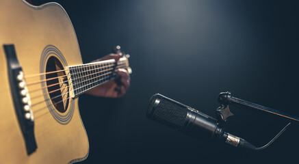 Male musician playing acoustic guitar behind microphone in recording studio.