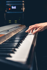 Fototapeta na wymiar A man's hand plays the piano keys in a dark interior of a music studio.
