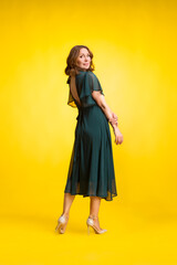 Elegant fashion. Stunning woman in elegant long dress in studio stands on a yellow sunny background.