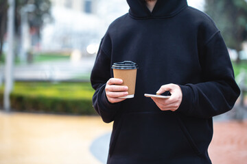 Man holding paper cup and smartphone outdoors.