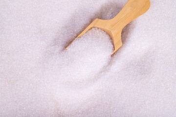 White granulated sugar. Top view wooden spoon inside heap of white refined sugar