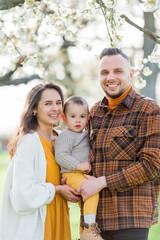 Happy young family with little son walks in blooming garden. Mom and dad with 1 year old baby. Spring.