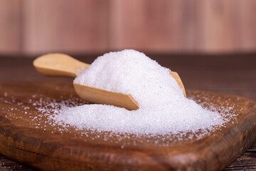 Fototapeta na wymiar White refined sugar on wood background. Close-up of granulated sugar in wooden spoon