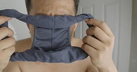 Asian man holding underpants and sniffing smell close-up.