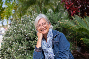 Portrait of senior white-haired woman sitting in outdoor garden under the sun relaxing looking at camera smiling