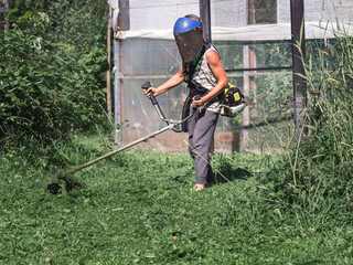 A teenager cuts the grass with a trimmer.