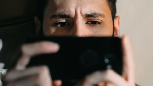 Phone movie. Gadget fatigue. Digital insomnia. Tired worried disturbed scared man face eyes watching drama thriller video show on electronic device.