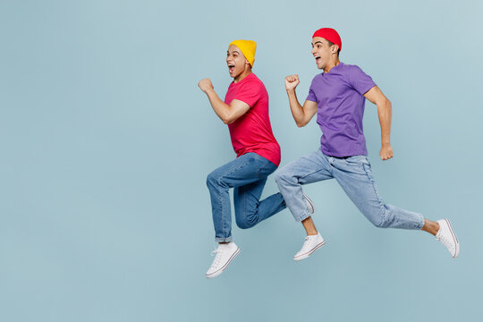 Full body sideways profile fun happy young couple two friends men wear casual clothes together jump high run fast hurry up in rush isolated on pastel plain light blue cyan background studio portrait.