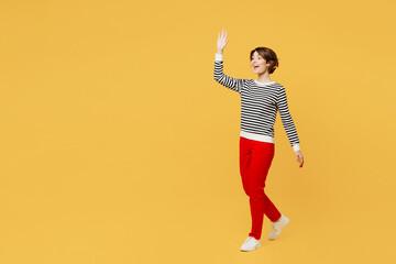 Fototapeta na wymiar Full body smiling happy fun young woman wear casual black and white shirt walking going strolling look camera waving hand isolated on plain yellow color background studio portrait. Lifestyle concept.