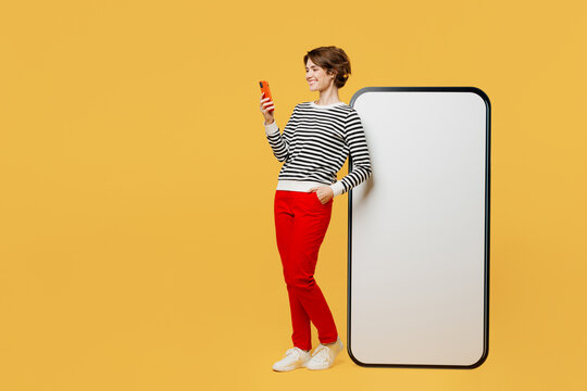Full body happy fun cheerful young woman wear casual black and white shirt big huge blank screen mobile cell phone with workspace mockup area using smartphone isolated on plain yellow color background