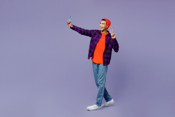 Full body young man of African American ethnicity wear casual shirt orange hat do selfie shot on mobile cell phone post photo on social network show v-sign isolated on plain purple color background