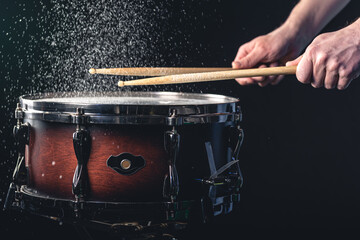 Obraz premium Drummer using drum sticks hitting snare drum with splashing water.