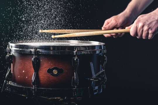Drummer using drum sticks hitting snare drum with splashing water.