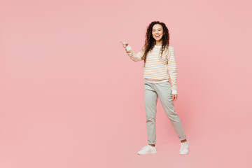 Fototapeta na wymiar Full body side view happy young woman of African American ethnicity she wear light casual clothes walking going strolling point finger aside isolated on plain pastel pink background studio portrait.