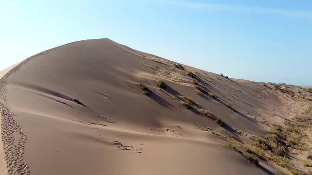 The Singing Dune is a beautiful landscape place that looks like a desert. Behind is the river. There are many bushes and traces of animals and people around. Altyn Emel, Kazakhstan. A huge sandy hill