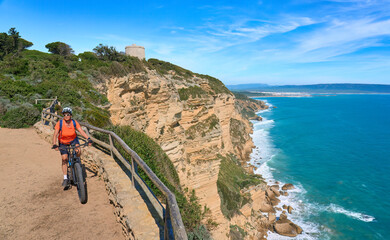 Happy senior woman cycling with her electric mountain bike on the cliffs of Cape Trafalgar, Costa de la Luz, Andalusia, Spain