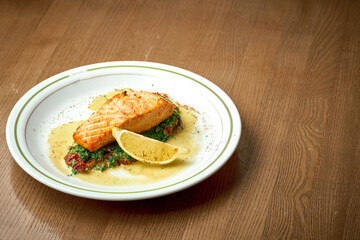 Salmon steak with spinach and yellow sauce in a plate on a wooden background.
