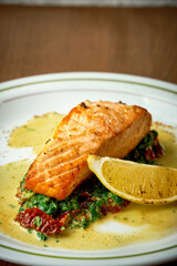 Salmon steak with spinach and yellow sauce in a plate on a wooden background.