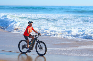 Happy senior woman cycling with her electric mountain bike at the beach of Cape Trafalgar, Costa de...