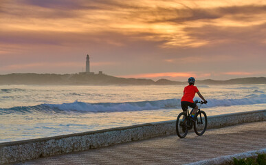 Happy senior woman cycling at sunset with her electric mountain bike at the beach of Cape...