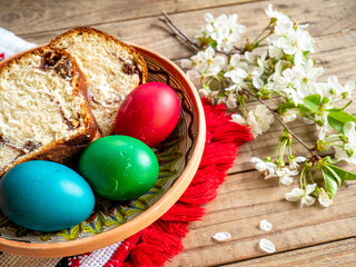 red Easter eggs next to flowering branches and plate with sweet sponge cake or cozonac on wooden table