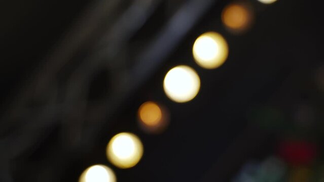 Blurred image of row of warm colored halogen lamps flickering and fading. Light fixture is mounted on ramp and is illuminated by beams of cold light from spotlights. Handheld shot.