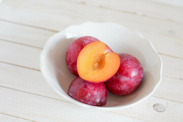 Seasonal fruit plum in white plate on white wooden background close up selective focus