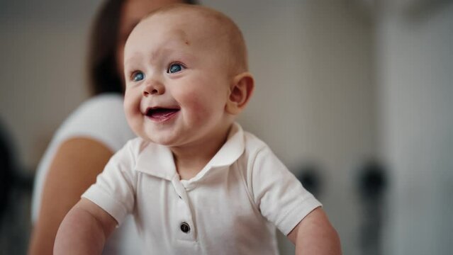 Portrait of active happy cute laughing smiling baby boy at home with mother. Babyhood, childhood motherhood parenting. Mom is babysitting in maternity leave. Raising child, kid and babycare concept.