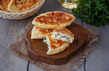 Traditional homemade fried cheese pies or pirozhki made from ricotta dough and filled with white cheese and herbs. Selective focus, horizontal, wooden background. © Iryna