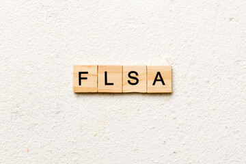 FLSA word written on wood block. Fair Labor Standards Act text on table, concept