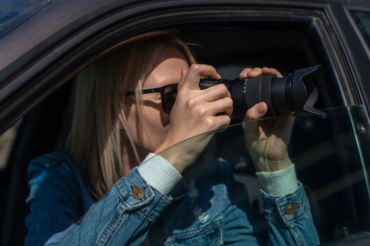 Woman in sunglasses with a camera sits in a car and takes pictures with a professional camera, a private detective or a paparazzi spy. Journalist is looking for sensations and follows celebrities.