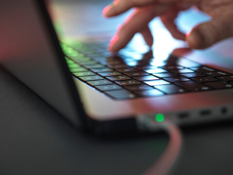 Hands typing on illuminated laptop keyboard in dark at home office