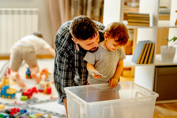 Father and son looking for toys in plastic container at home
