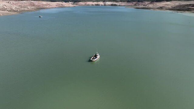 Fishing boats on Sau dam with low water level, Catalonia. Aerial tilt up descending