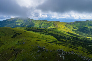 Fototapeta premium Scenic aerial view of the foggy Carpathian mountains, village and blue sky with sun and clouds in morning light, summer rural landscape