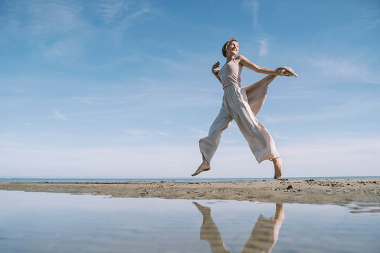 Reflection of happy woman jumping at beach - Powered by Adobe