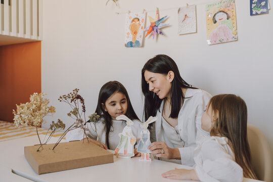 Mother and daughters playing with paper Easter bunnies at home