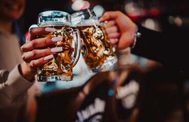 man and woman hands clinking with glasses of beer in bar