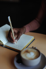 Cropped photo of African-American woman wearing pink sweater, sitting at beige wooden table with...