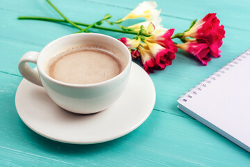 Blank notepad, coffee cup on turquoise wooden table with freesia flowers. Mothers day concept. Top view