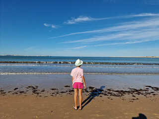 Girl with hat in front of the sea, on a sandy beach. Valdelagrana Beach