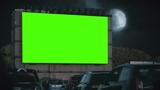 Moonlight Drive In Theater Green Screen Cinema Exterior Night Cars Parked. green screen in a drive in theater at night with cars parked watching movie. Full moon, cloudy sky