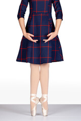 En Pointe heels together hands bras bas looking down teachers persepctive Young female ballet dancer on white background tartan dress pink silk and satin pointe shoes
