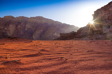 Wadi Rum w Jordanii. Zbliżenie na pustynny piasek na tle skalnych gór oświetlonych słońcem.