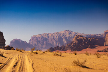 Wadi Rum w Jordanii. Pustynna droga wiodąca do skalnych gór. - obrazy, fototapety, plakaty