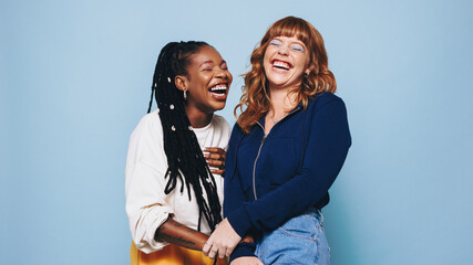 Funny best friends laughing cheerfully while standing together in a studio - obrazy, fototapety, plakaty