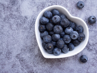 Top view, fresh blueberries in heart-shaped white plate on dark grey background. Flat lay with copy...