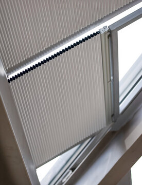 Motorized pleated blinds on the roof windows. Cellular pleated blinds for skylights, beige color. Honeycomb curtains on glass roof. Selective focus.