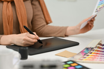Young creative woman using graphic tablet and working with color swatch samples at modern workplace